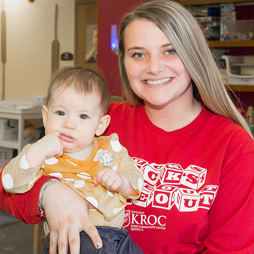 A White Caucasian Female Smiling While Holding a Baby | Kroc Center Membership