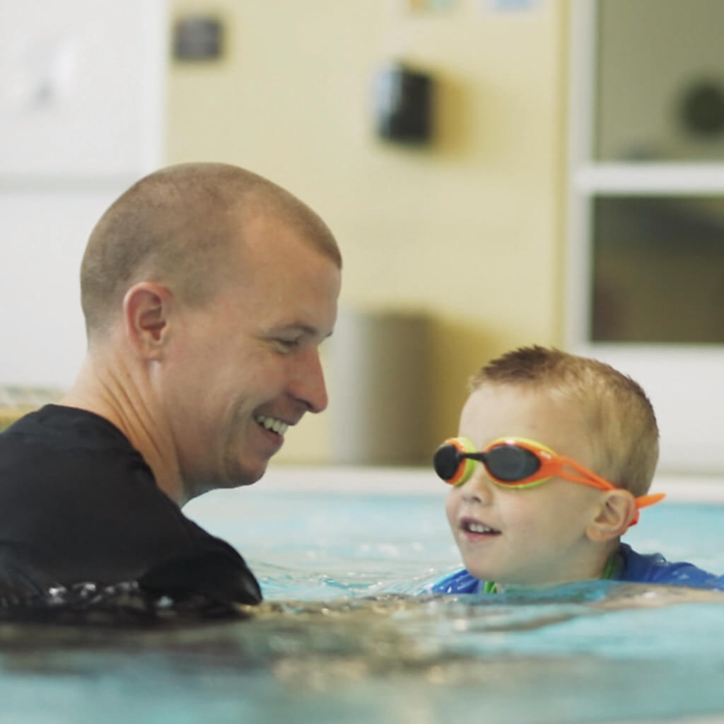 A Male Trainer Assisting a Young Boy in Goggles To Swim | Kroc Center Quincy, IL